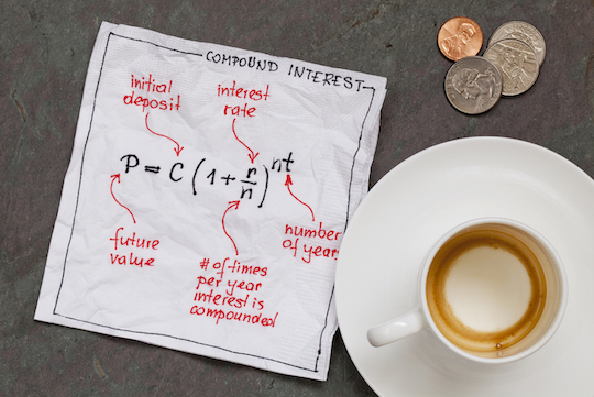 Image is of a table top with an empty coffee cup, a few coins and a napkin with writing on it. The writing is about compounding interest with an equation for how to calculate it.